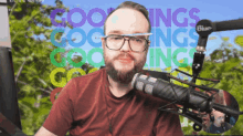 a man wearing glasses stands in front of a microphone in front of a colorful background that says coolings coolings coolings
