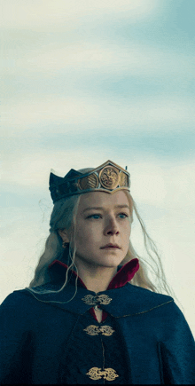 a woman wearing a crown and a cape looks at the camera