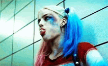 harley quinn from suicide squad is standing in front of a wall with her tongue sticking out .