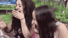 two women are laughing and covering their mouths with their hands .