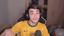 a man wearing headphones and a yellow shirt is sitting in front of a microphone .