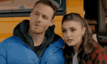 a man and a woman standing next to each other in front of a yellow vehicle