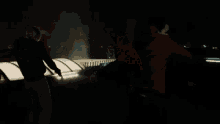 a man and a woman are standing on a rooftop at night looking at a city .