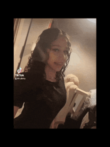 a girl with curly hair is wearing a black shirt and has a tiktok on her phone