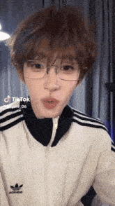 a person wearing glasses and an adidas jacket