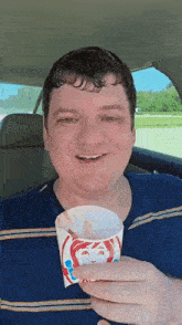 a man in a blue shirt is holding a cup of wendy 's ice cream .