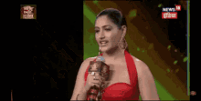 a woman in a red dress is holding a microphone in front of a news 18 screen