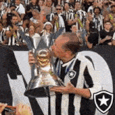 a man in a striped shirt kisses a trophy in front of a crowd