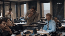 a man smoking a cigarette in an office with a max logo on the bottom