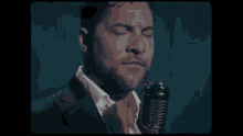 a man in a suit and white shirt is singing into a microphone with his eyes closed .