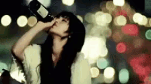 a woman is drinking a bottle of wine in front of a blurry background