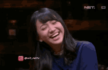 a woman in a blue shirt is smiling in front of a screen that says net .