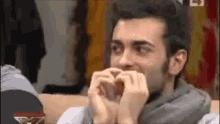 a man is making a heart shape with his hands in front of his face .
