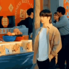 a man in a tan jacket is standing in front of a chinese restaurant .