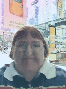 a woman wearing glasses stands in front of a large sign that says small decision big impact