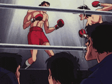 a man in red shorts is boxing in a ring with other men watching