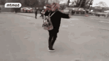 a person with a backpack is walking down a street with their arms outstretched .