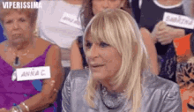 a woman with blonde hair is sitting in a crowd of people with a name tag that says anna c.