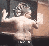 a naked man is standing in front of a dart board with the words `` i am in '' written on the bottom .