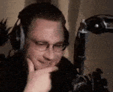 a man wearing headphones and glasses is sitting in front of a microphone and making a funny face .