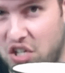 a man with a beard is making a funny face while holding a cup of coffee .