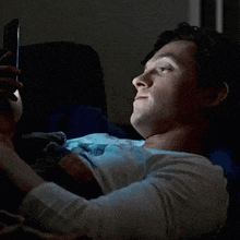 a woman is laying on a bed looking at her phone and making a funny face .