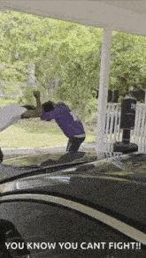 a man in a purple shirt is fighting another man in a white shirt in front of a house .