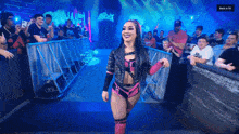 a woman in a pink and black outfit is walking in front of a crowd with the words back in 55 at the bottom
