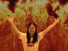 a girl wearing a white shirt with a picture of a car on it stands in front of a fire background