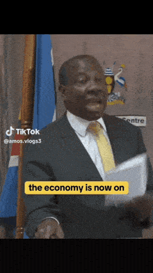 a man in a suit and tie is giving a speech and the economy is now on