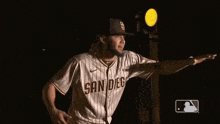 a baseball player in a san diego jersey is standing in front of a traffic light in the dark .
