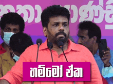 a man in a red shirt stands in front of microphones with a sign that says ' gm '