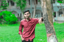 a man in a red shirt leans against a tree in a park