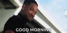a man is smiling and says `` good morning '' while standing in front of a building .