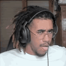 a man with dreadlocks wearing headphones and glasses sticks his tongue out