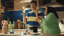 a man in a blue and yellow striped shirt stands next to a woman in a kitchen