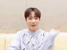 a young man is sitting on a couch wearing a blue sweater and a necklace .