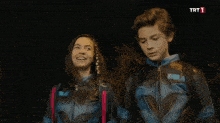 a boy and a girl are standing next to each other with a trt 1 logo behind them