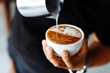 a person is pouring milk into a cup of coffee with a picture of two people on the foam