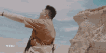 a man with his arms outstretched is standing in front of a rocky cliff