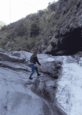 a woman is walking down a rocky cliff near a waterfall