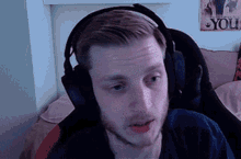 a man wearing headphones looks at the camera with a poster on the wall that says ' one piece ' on it