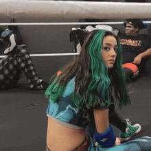 a woman with green hair is sitting in a boxing ring with a man wearing a shirt that says worldly
