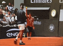a man holds up a tennis ball in front of a sign for infosys