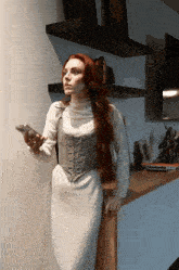 a woman with long red hair is leaning on a counter holding a remote control
