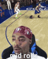 a man wearing a bandana is sitting on a basketball court watching a game .