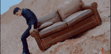 a man is leaning on a brown couch in the sand .