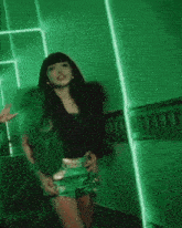 a woman in green shorts and a black top is standing in front of a green wall .