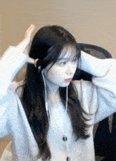 a girl wearing ear buds and a white sweater is sitting in a chair