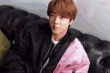 a young man wearing a black jacket and a pink jacket is sitting on a black leather couch